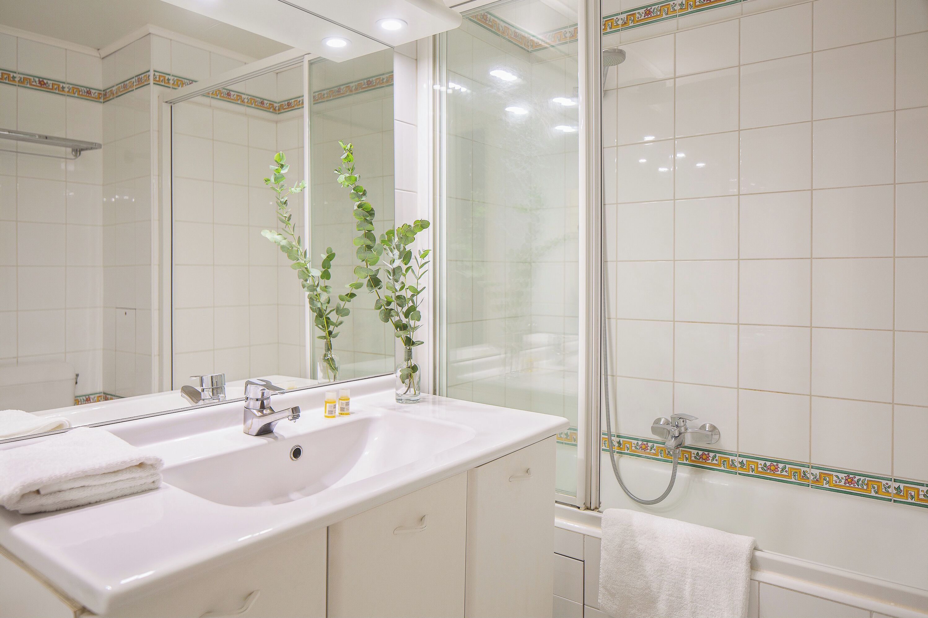 Une salle de bain avec un lavabo blanc, deux miroirs, une cabine de douche en verre et un porte-serviettes.