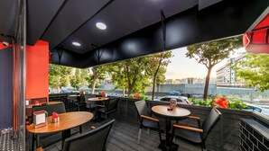An outdoor seating area with tables and chairs, a view of the city, and a red wall. - Dem İstanbul Airport Hotel (Istanbul)