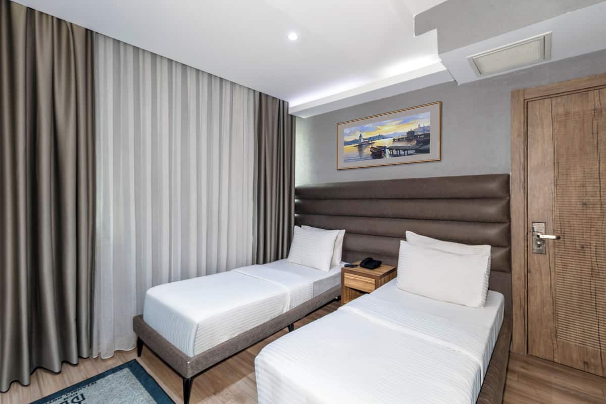 Quarto de hotel com duas camas, uma porta de madeira, um quadro na parede e uma mesa de cabeceira com um telefone.