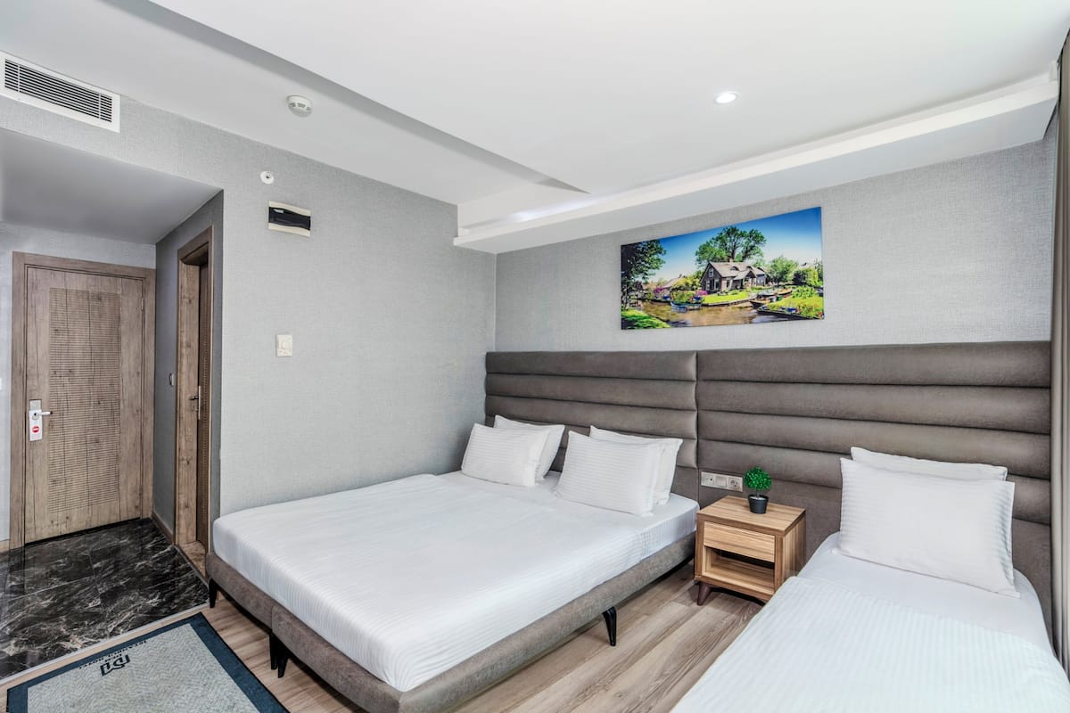 Quarto de hotel com duas camas, um quadro na parede e uma pequena planta na mesinha de cabeceira.