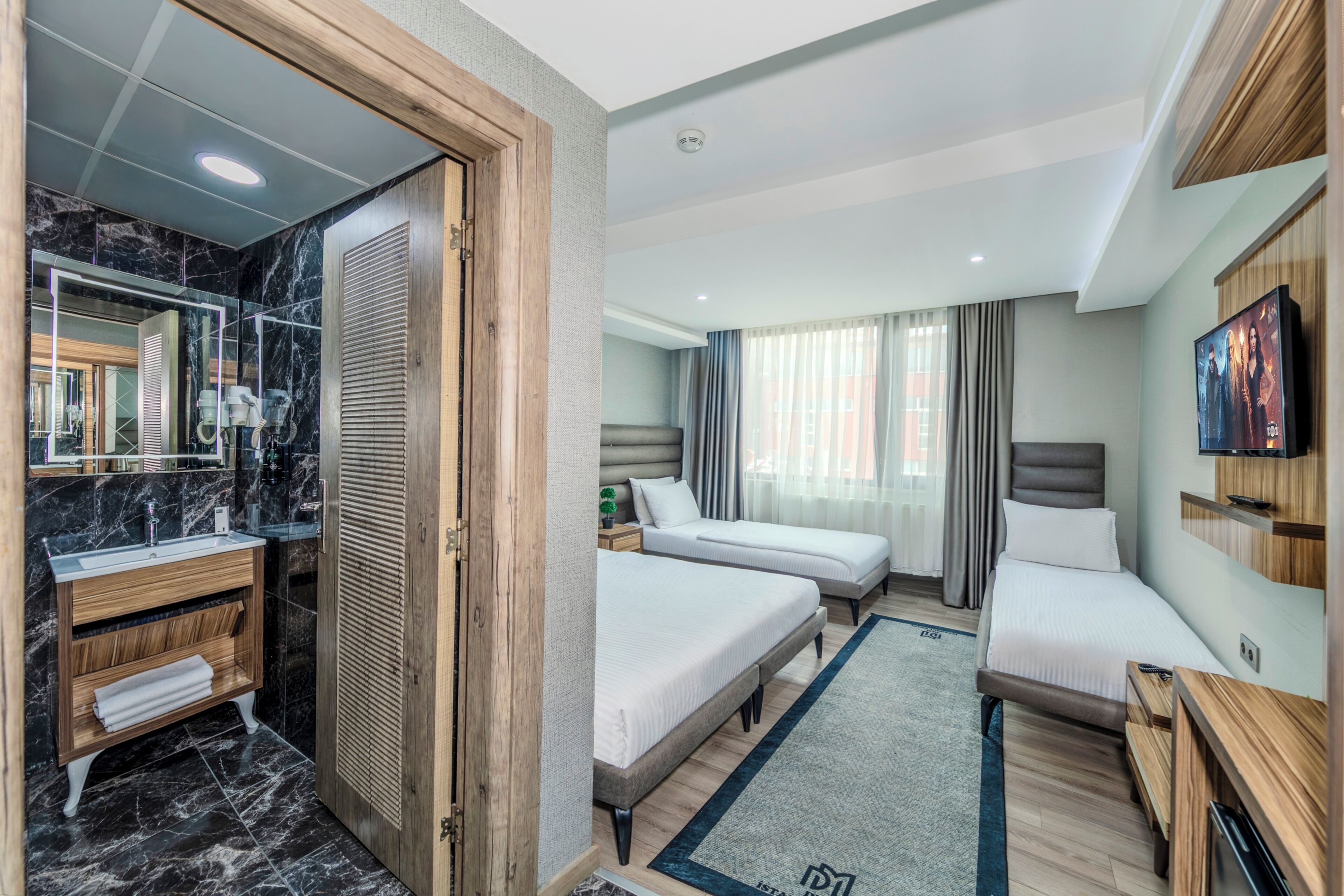 Una habitación de hotel con baño, dos camas, televisión y un espejo grande.