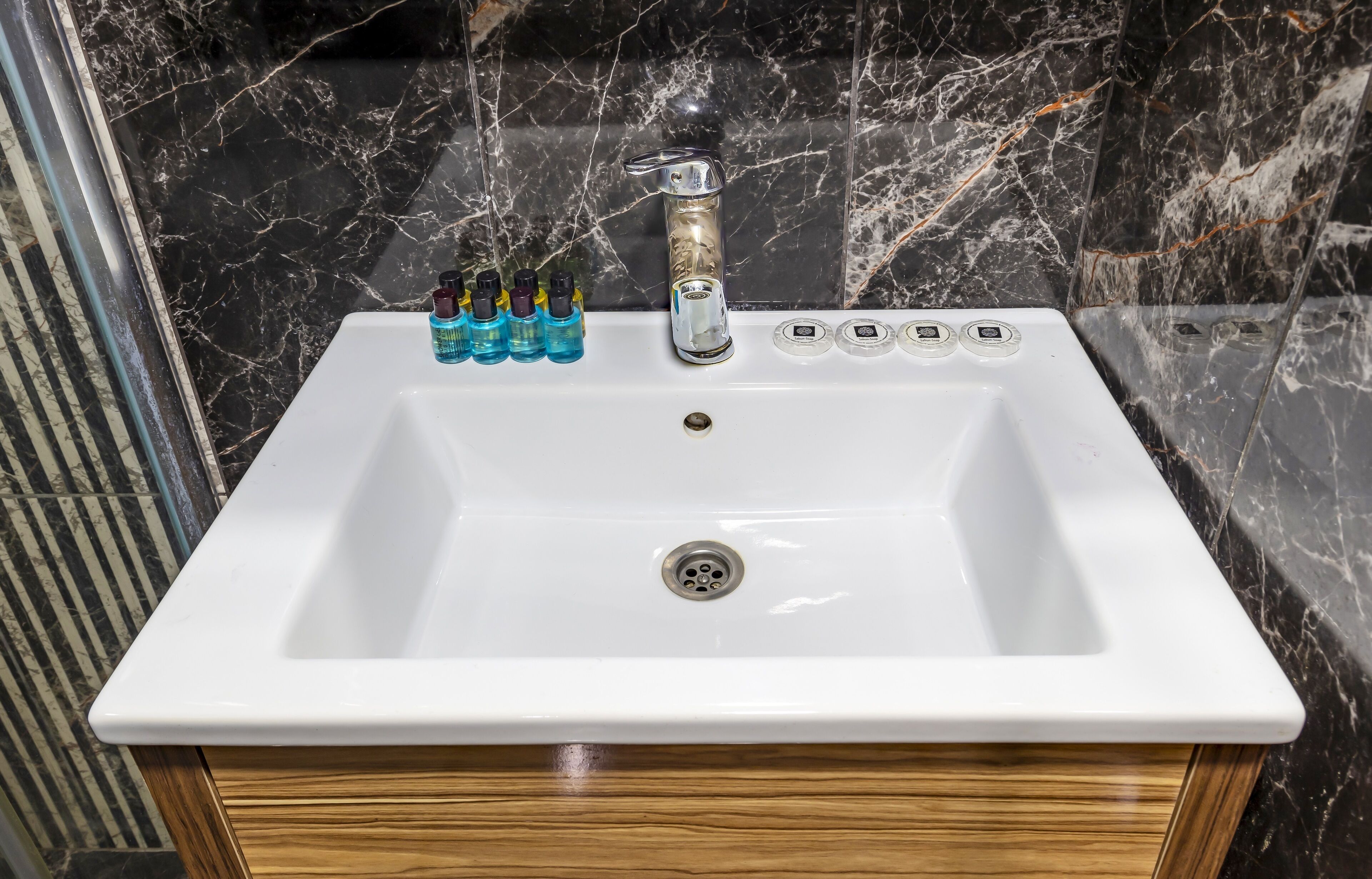A white bathroom sink with a marble backsplash, a faucet, and a row of toiletries.
