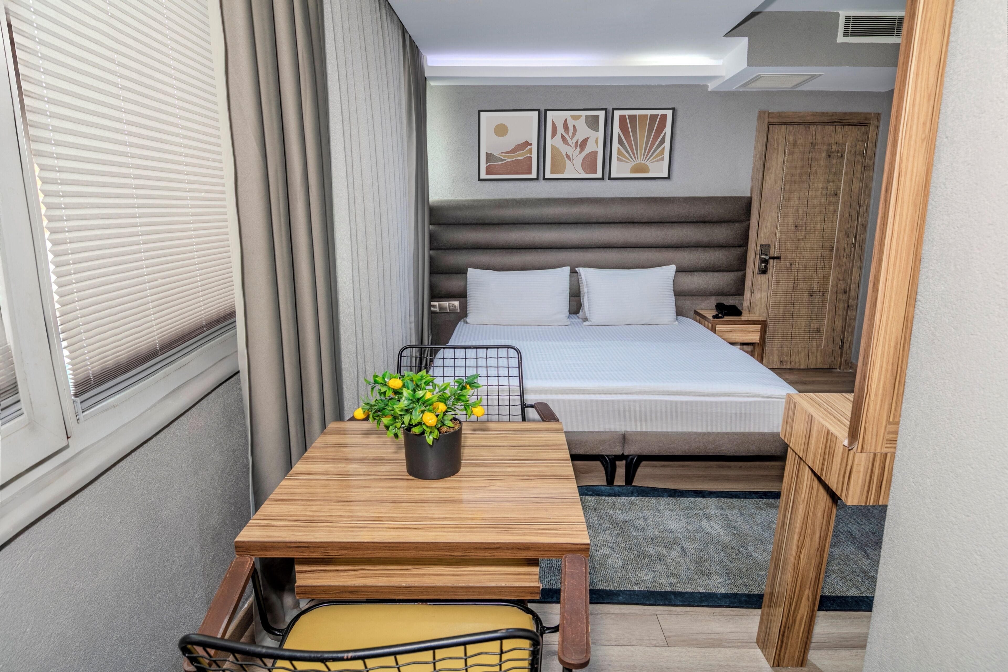 A compact hotel room with a bed, bedside table, and a small window with blinds.