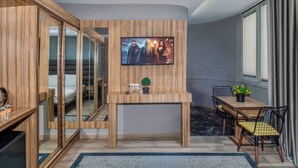 A modern room with a TV mounted on a wooden wall, a small table with a plant, and a seating area with chairs. - Dem İstanbul Airport Hotel (Istanbul)