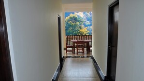 Un pasillo con un banco y una mesa al final, que conduce a un balcón con vistas a árboles.