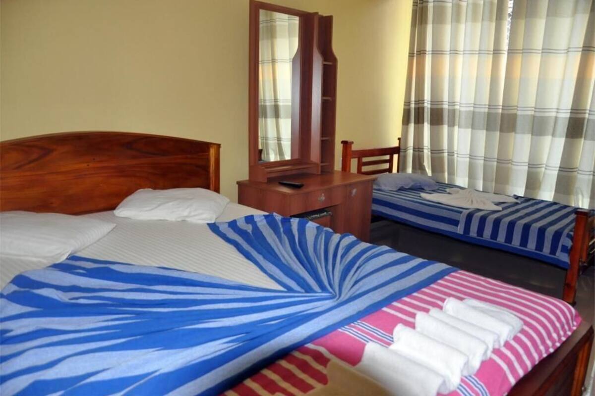 A room with two beds, a wooden headboard, a mirror, a wooden desk, and a window with curtains.
