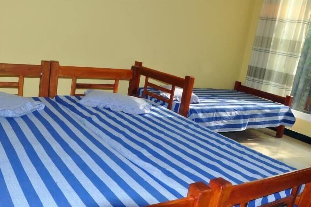 A room with two beds, each with a wooden headboard and blue-striped bedding.