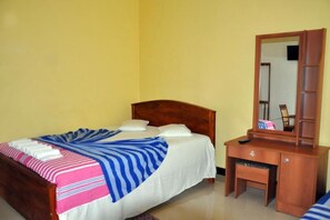 A single bed with a wooden headboard, a bedside table with a mirror, and a bench at the foot of the bed. - Hotel Pearl Gate (Chilaw)