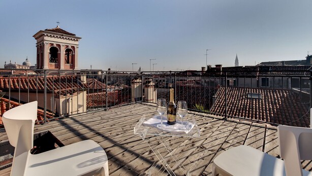 A rooftop terrace with a table set for two, overlooking a cityscape with terracotta roofs and a bell tower. - Venice Skyline View Sudio Apartment (Venice)