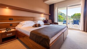 A modern hotel room with a large bed, wooden headboard, bedside table with a phone, and a view of the outdoors through a sliding glass door. - Hotel Plaza Omis (Omis)