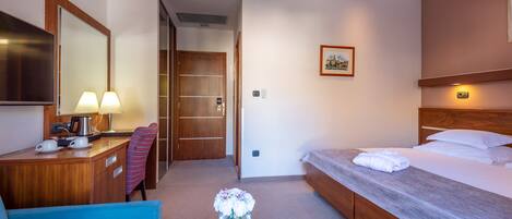 Habitación de hotel con cama, escritorio con lámpara, silla, una mesita con un florero y un cuadro en la pared.