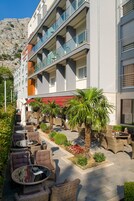 Hotel com área externa para sentar, palmeiras e montanhas ao fundo.