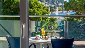 A balcony with a table set for breakfast, overlooking a coastal area with trees and buildings. - Hotel Plaza Omis (Omis)