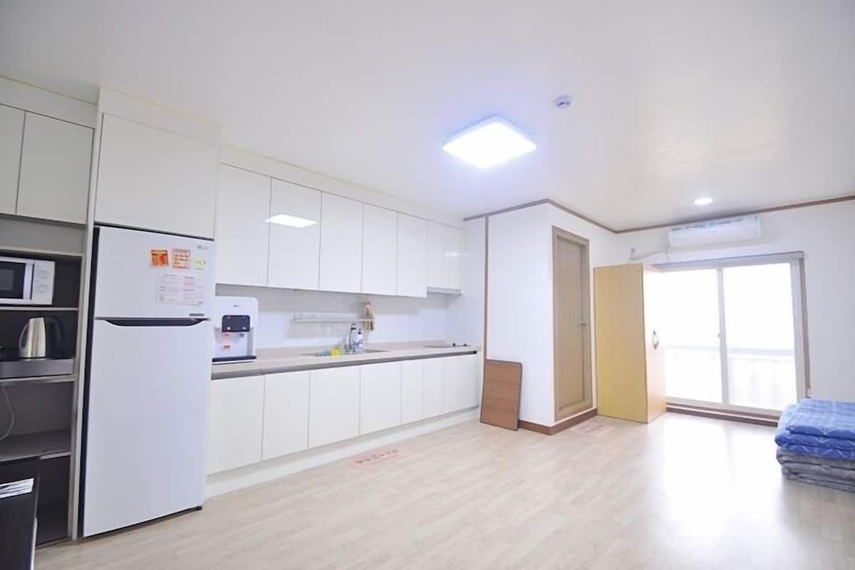 A modern kitchen with white cabinets, a refrigerator, and a coffee machine. There is a sliding glass door leading to a balcony.