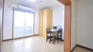 A room with a sliding glass door leading to a balcony, a wooden cabinet, a table with two chairs, and a microwave. - Osio Pension (Jeju City)