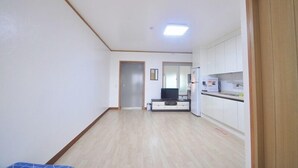 A narrow hallway with a wooden floor, white walls, and a door at the end. - Osio Pension (Jeju City)