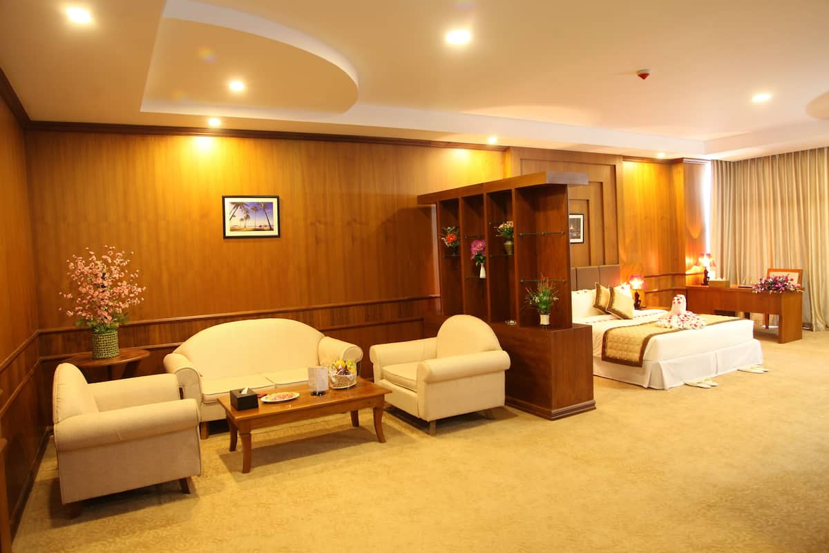 Quarto de hotel com parede de madeira, um sofá, uma cadeira, uma mesa pequena e uma cama com colcha branca.