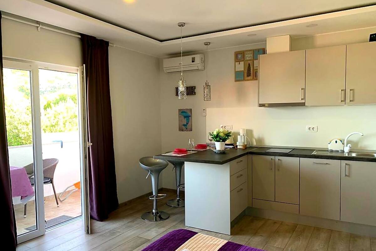 Una cocina moderna con una isla central, una zona de comedor con dos taburetes altos y un ventanal corredero que da a un patio exterior.