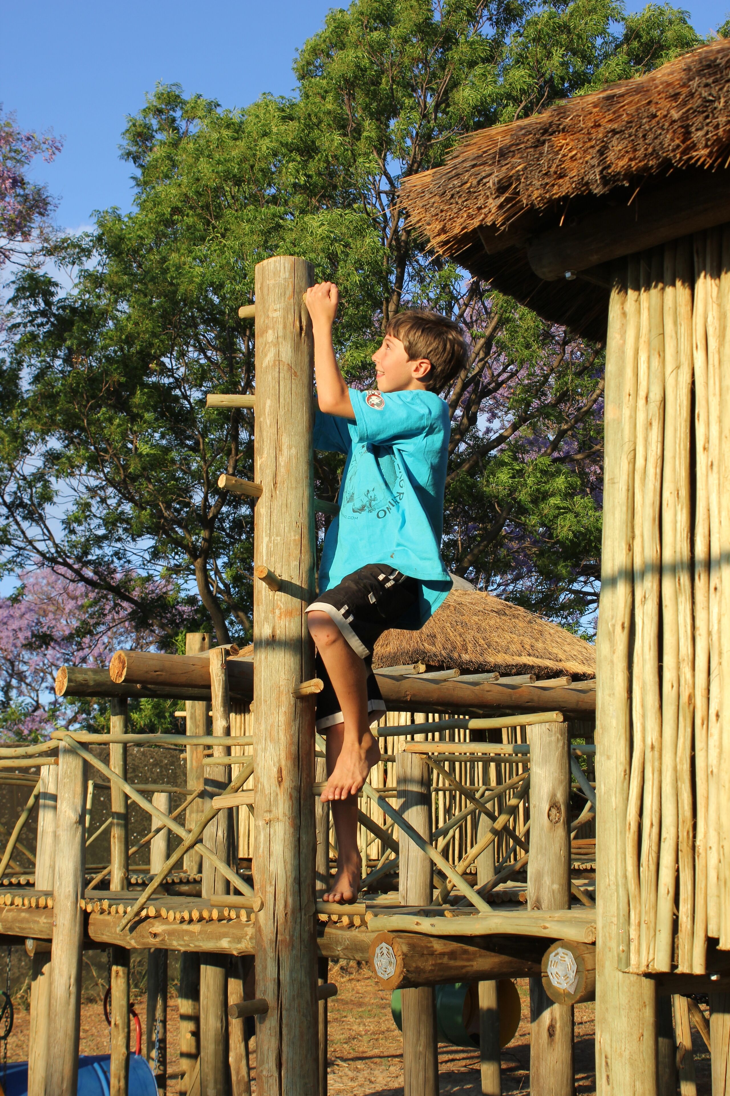 Un enfant qui grimpe sur une structure en bois surmontée d’un toit de chaume.