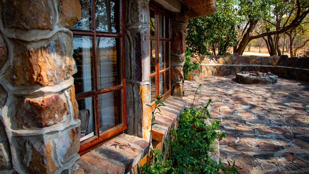 A stone building with large windows and a stone pathway leading to a seating area. - Waterberg Cottages (Vaalwater)