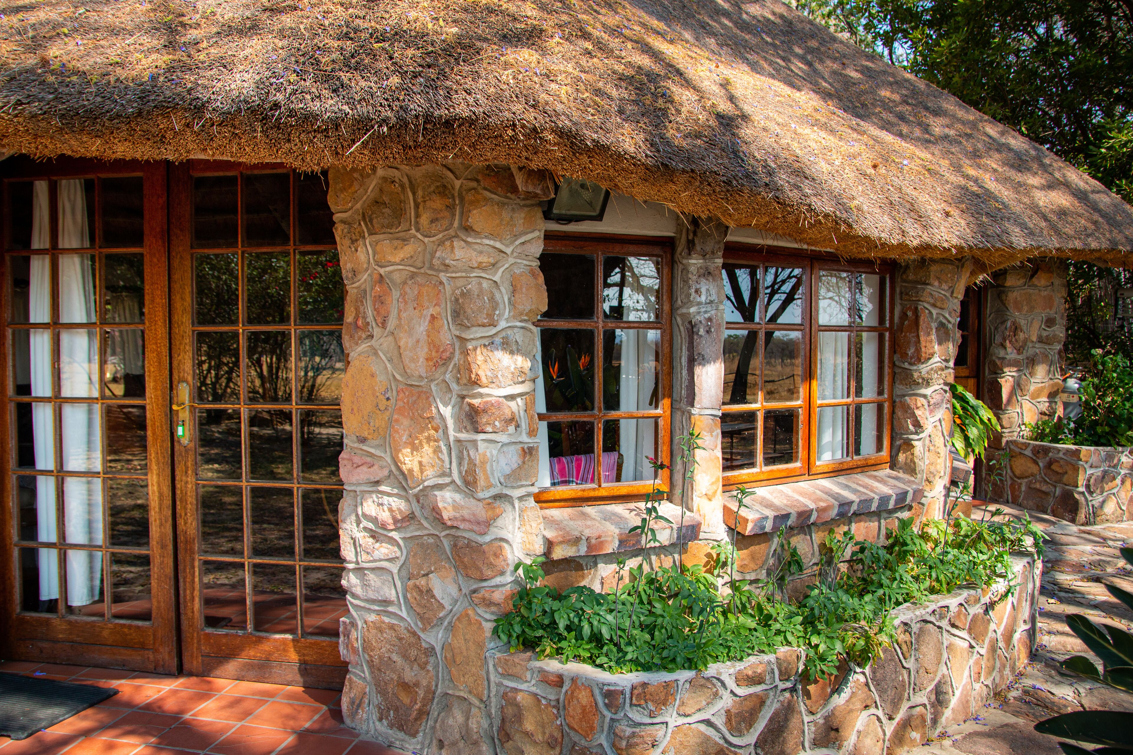 A stone house with a thatched roof, large windows, and a stone staircase leading to a porch.
