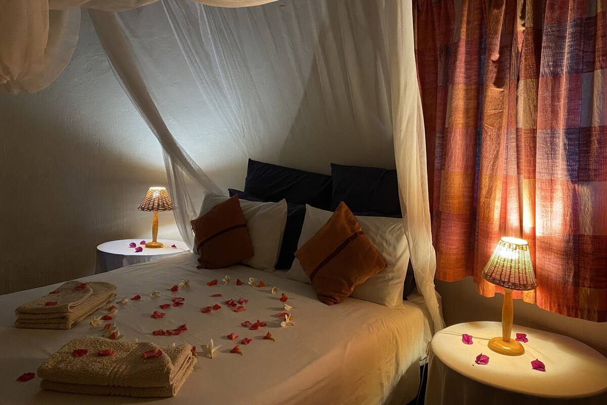 A bed with a canopy, pillows, a bedside table with a lamp, and towels.