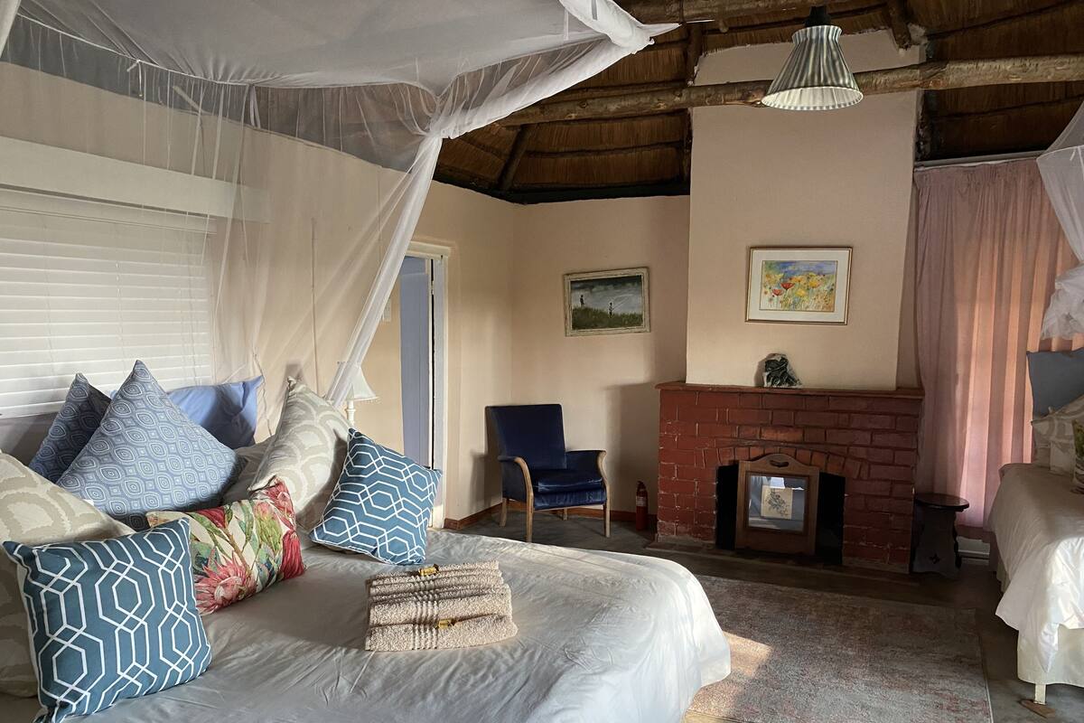 A bedroom with a bed, pillows, a chair, a fireplace, and a window with curtains.