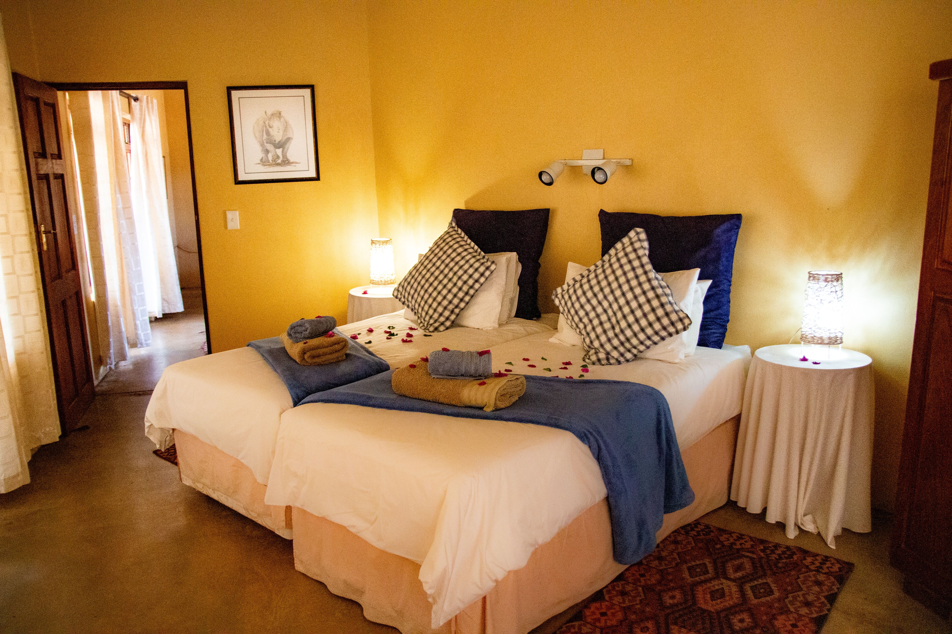A hotel room with two beds, a bedside table, a nightstand, a framed picture on the wall, and a patterned rug.