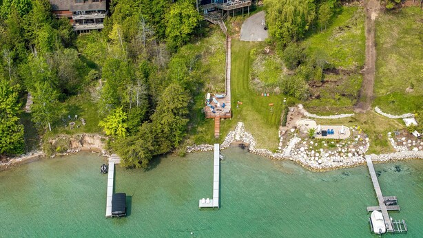 An aerial view of a lakeside property with a dock, a wooden deck, and a house surrounded by trees. - Waterfront Deck + Dock: Torch Lake Home! (Rapid City)