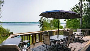 A deck with a grill, outdoor table and chairs, and a large umbrella. - Waterfront Deck + Dock: Torch Lake Home! (Rapid City)