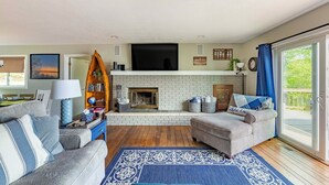A living room with a fireplace, sofas, a TV, and a large window. - Waterfront Deck + Dock: Torch Lake Home! (Rapid City)