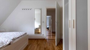 Un dormitorio con cama, armario, espejo y puerta que da a otra habitación.