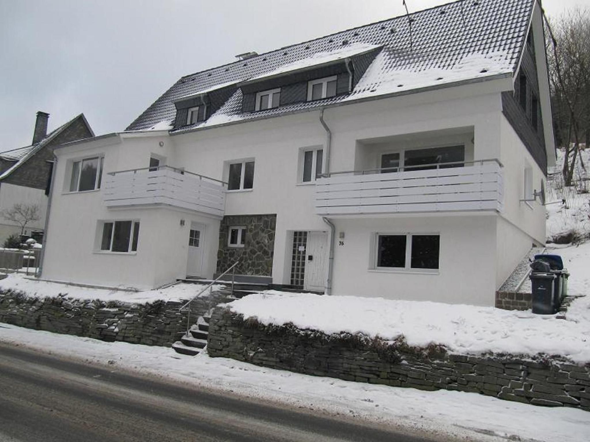 A two-story house with a stone foundation, a balcony on the second floor, and a front door.