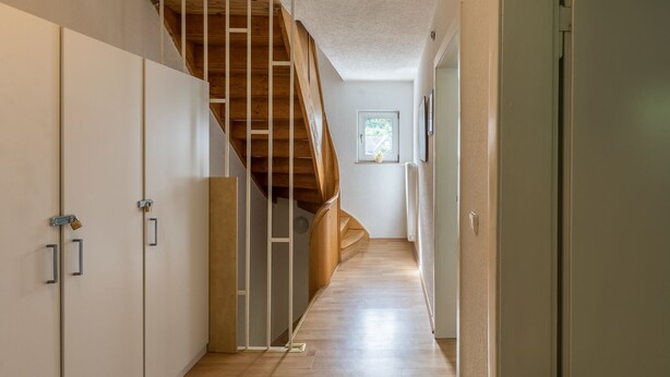 Un pasillo estrecho con una escalera de madera que sube a un segundo piso.