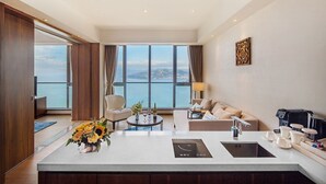 A modern hotel room with a large window offering a view of the sea, a central island with a sink and a coffee machine, a sofa, and a chair. - Argyle Resort Dali Yueyun (Dali)
