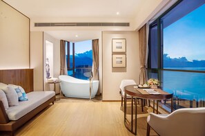 Habitación de hotel moderna con un amplio ventanal que ofrece vistas panorámicas, una bañera, un sofá y una mesa de comedor.