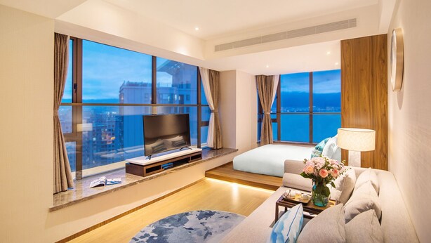 A modern hotel room with a large TV, comfortable seating, and large windows offering city views. - Argyle Resort Dali Yueyun (Dali)