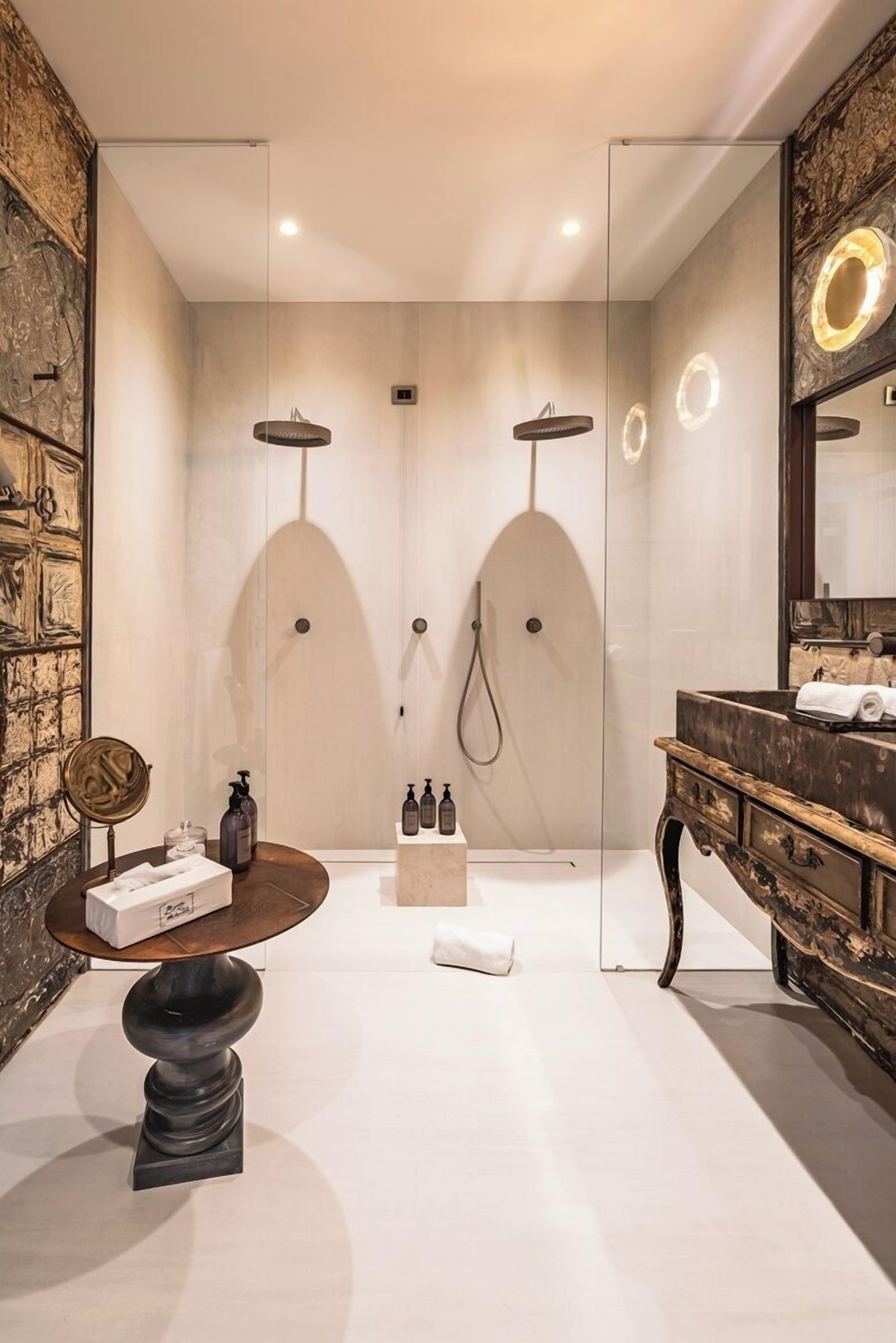 Un baño moderno con ducha de vidrio, tocador con espejo y una mesita con artículos de aseo.