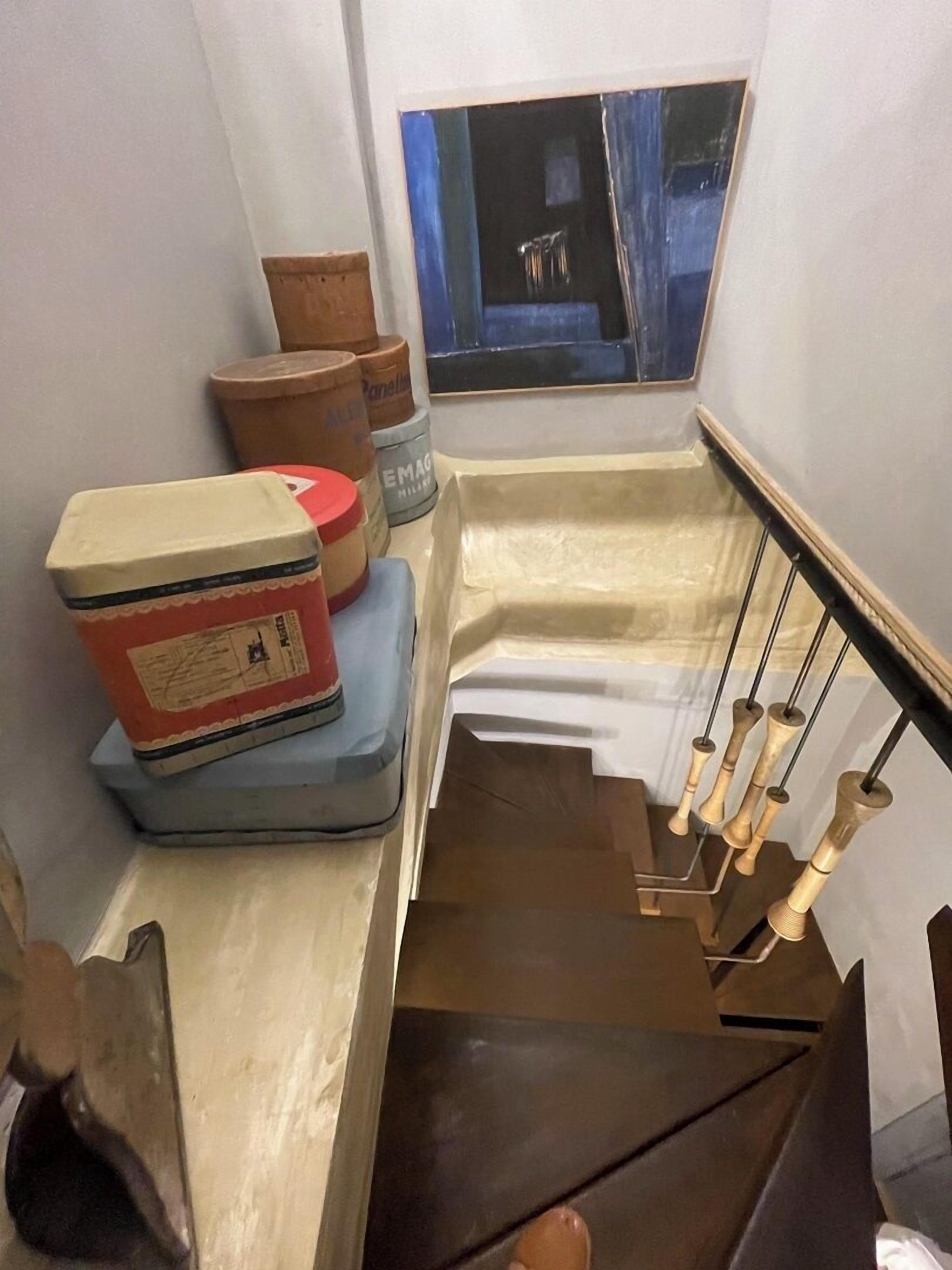 Een smalle trap met een leuning, houten treden en een raam bovenin.