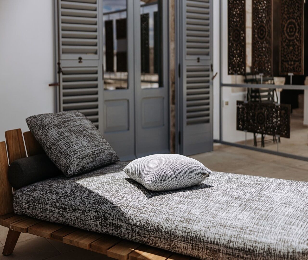Una cama individual con una colcha gris y blanca estampada y dos almohadas, un cabecero de madera y una puerta gris al fondo.