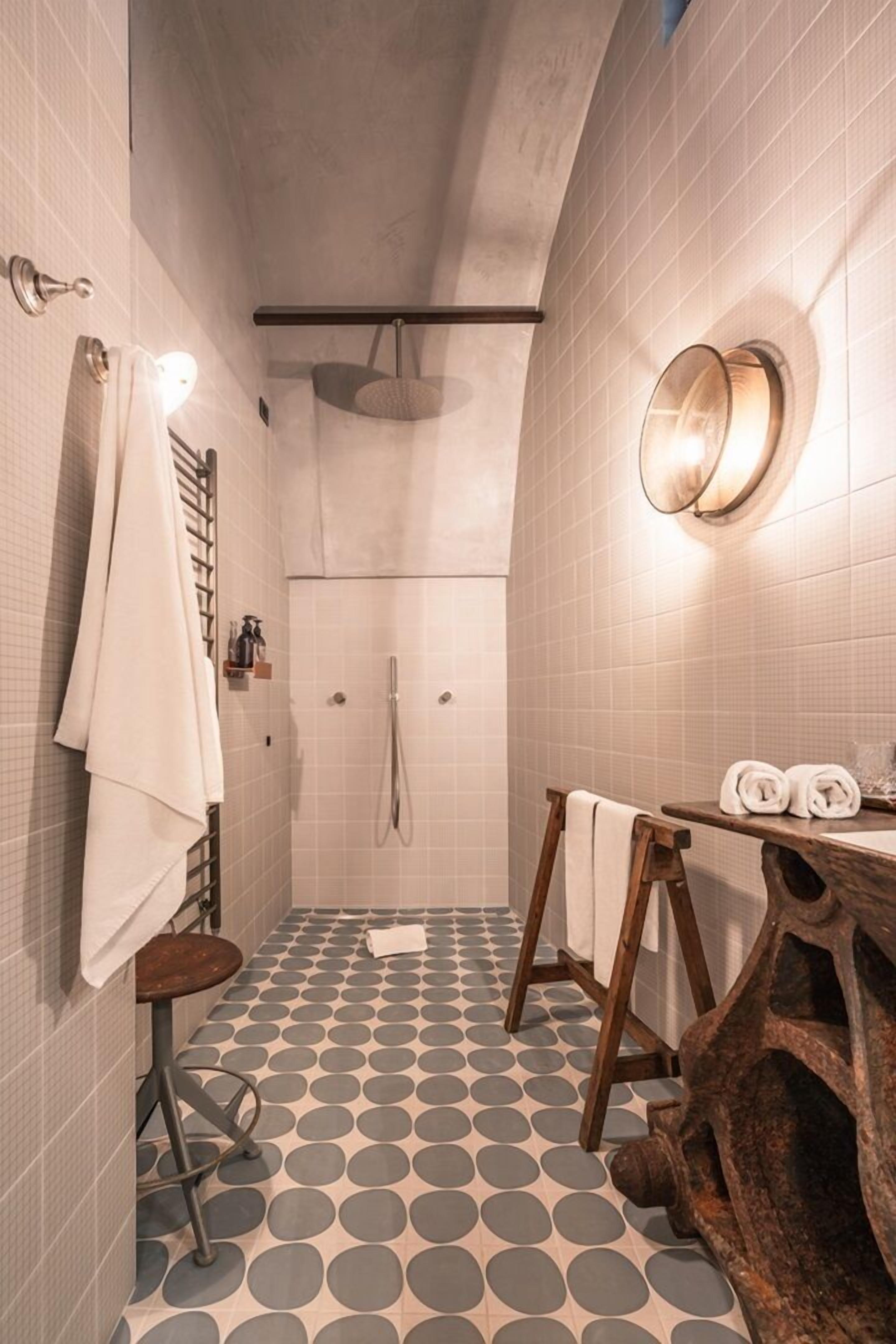 Un baño con ducha, un taburete de madera, un espejo redondo y un suelo con diseño.