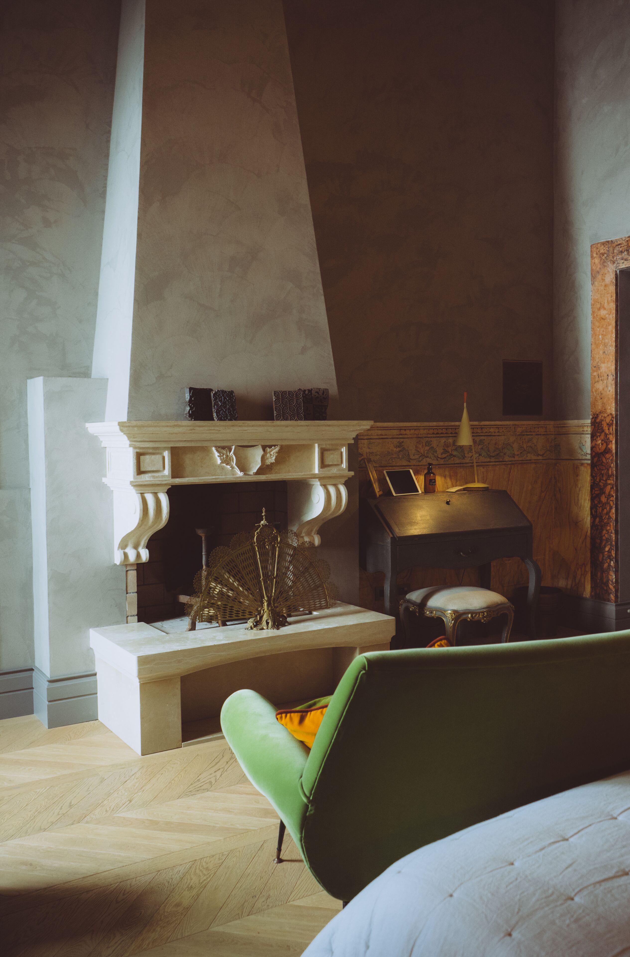 A room with a fireplace, a green armchair, a wooden desk, and a mirror.