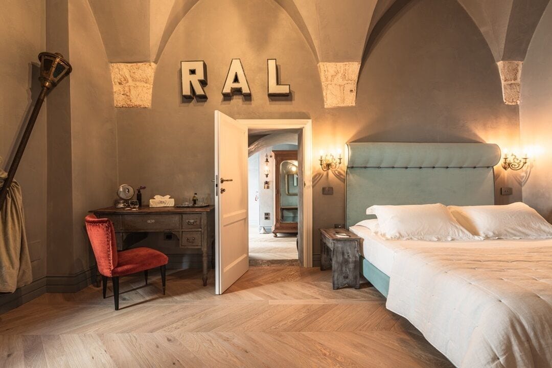 A bedroom with a bed, a desk, and a chair. There is a door leading to another room.