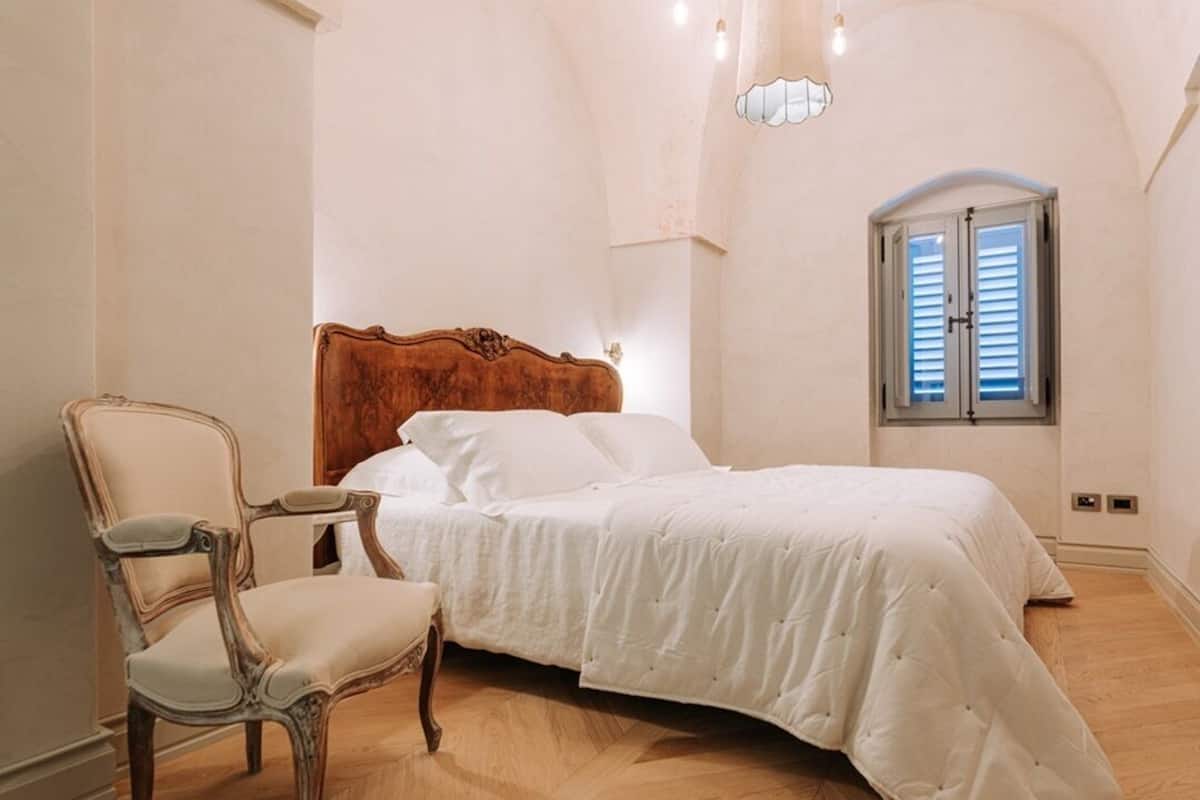 A bedroom with a wooden headboard, a white bedspread, and a wooden chair.