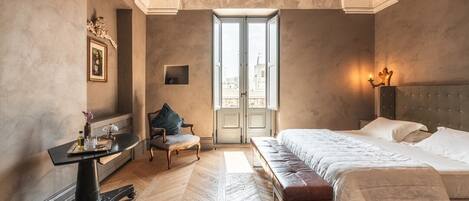 Un dormitorio con una cama grande, un escritorio y una silla. Se ve una ventana con vistas a edificios.