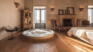 Un dormitorio amplio con una cama grande, una bañera redonda, una chimenea y un armario antiguo.