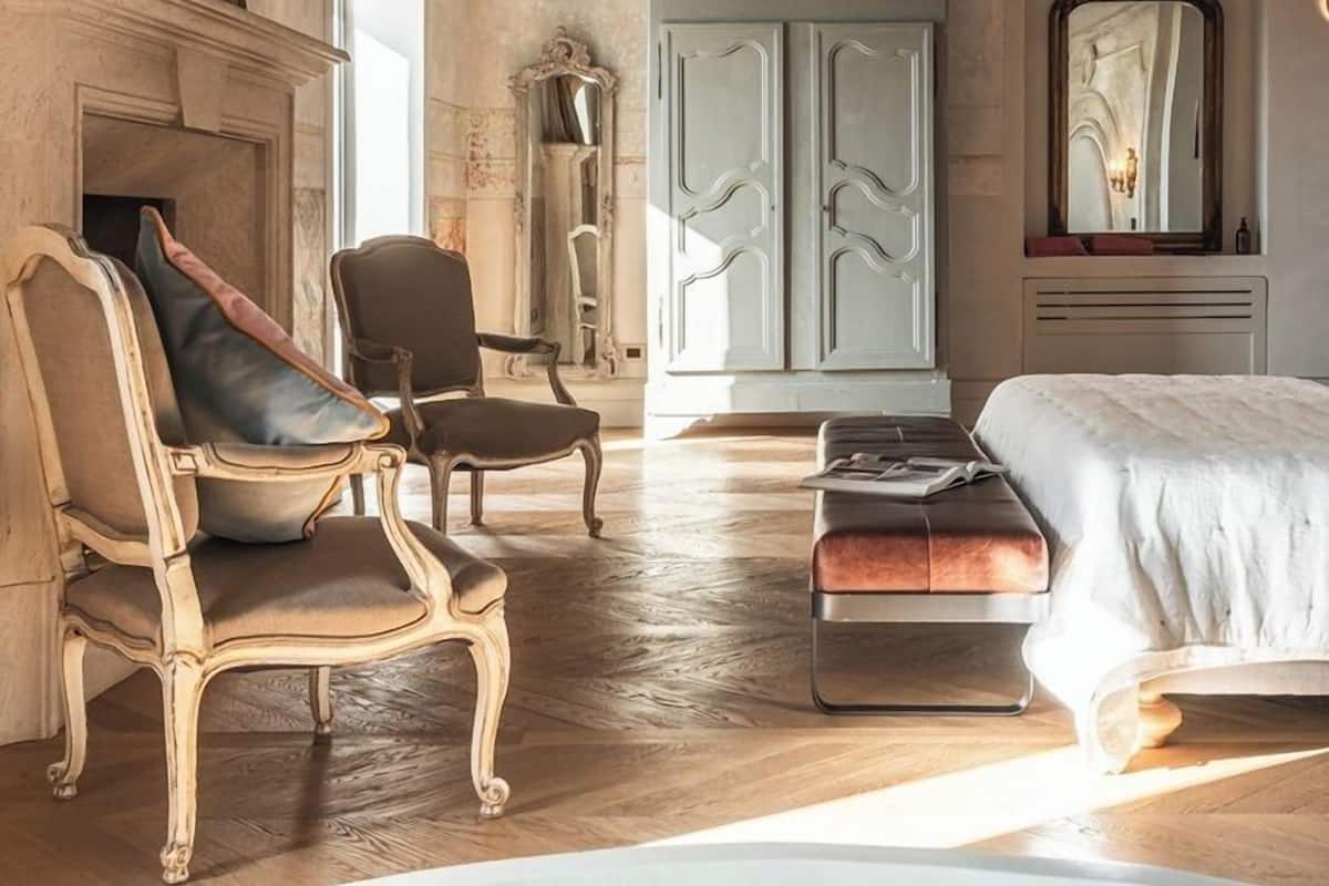 A spacious room with a large bed, two armchairs, a fireplace, and a wardrobe.
