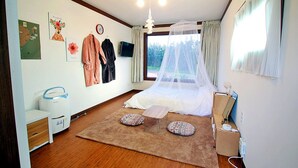 A bedroom with a bed, a bedside table, a chair, a window with curtains, a wall-mounted TV, and a map on the wall. - Wedding House (Seogwipo)