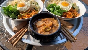 A meal consisting of two bowls of noodles with fried eggs, a bowl of soup, and condiments on a tray. - Wedding House (Seogwipo)