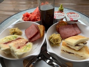 A table with two white plates containing sandwiches, ham, and a side of watermelon. There is also a bottle of strawberry yogurt and a glass of iced tea.